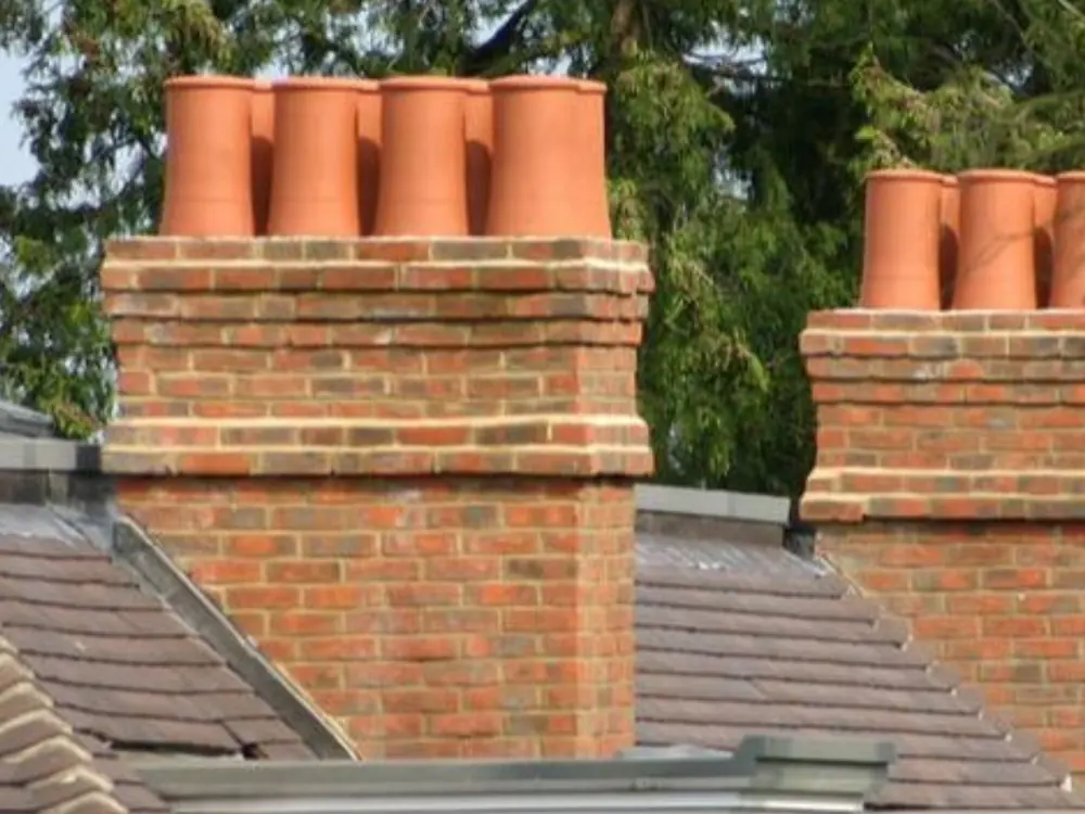 Two red brick chimney stacks with terracotta pots on a tiled roof