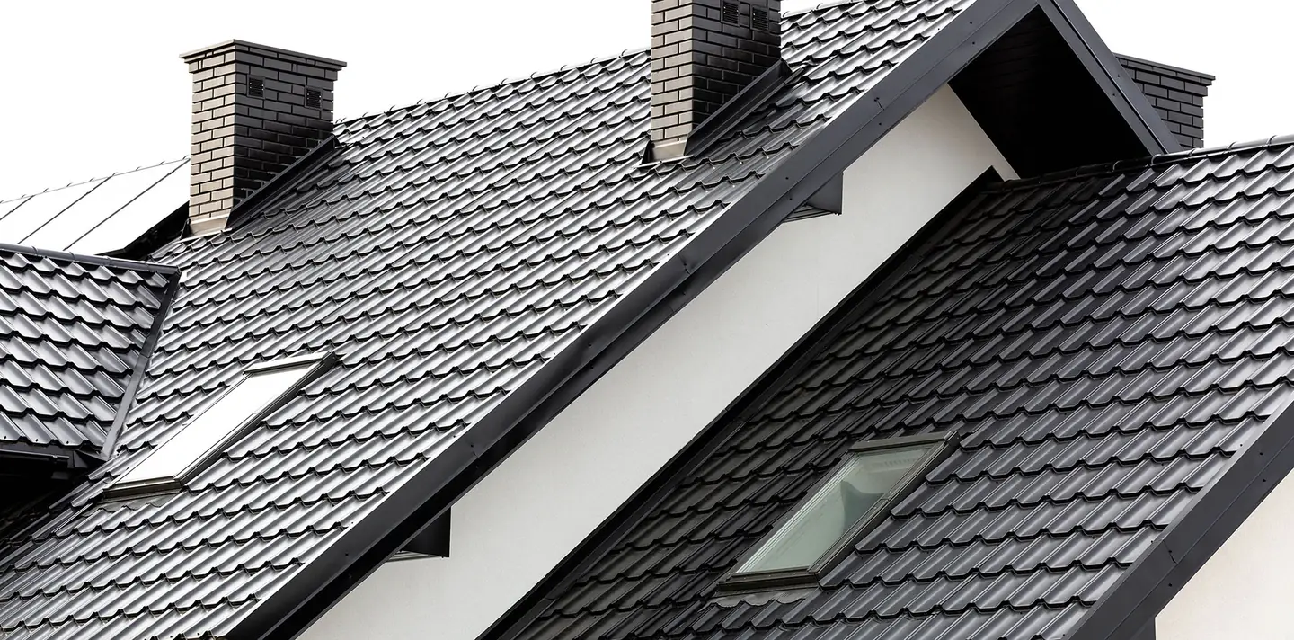 Dark grey tiled pitched roof with brick chimneys and roof windows