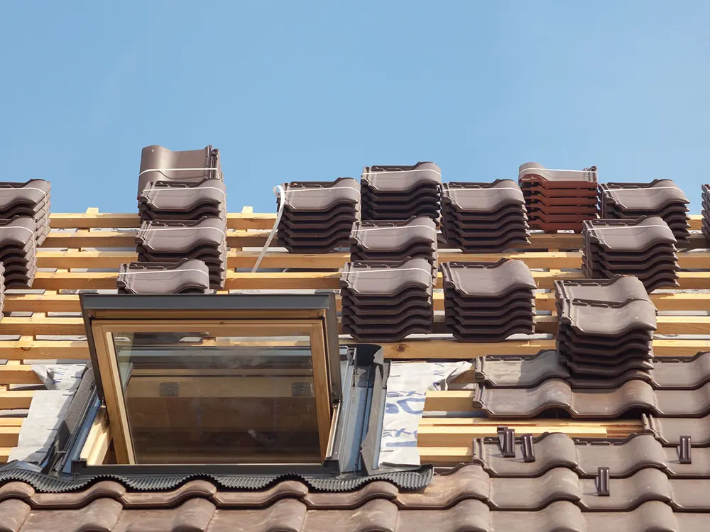 Pitched roof part way through re-tiling, with new tiles stacked on the battens beside a roof window